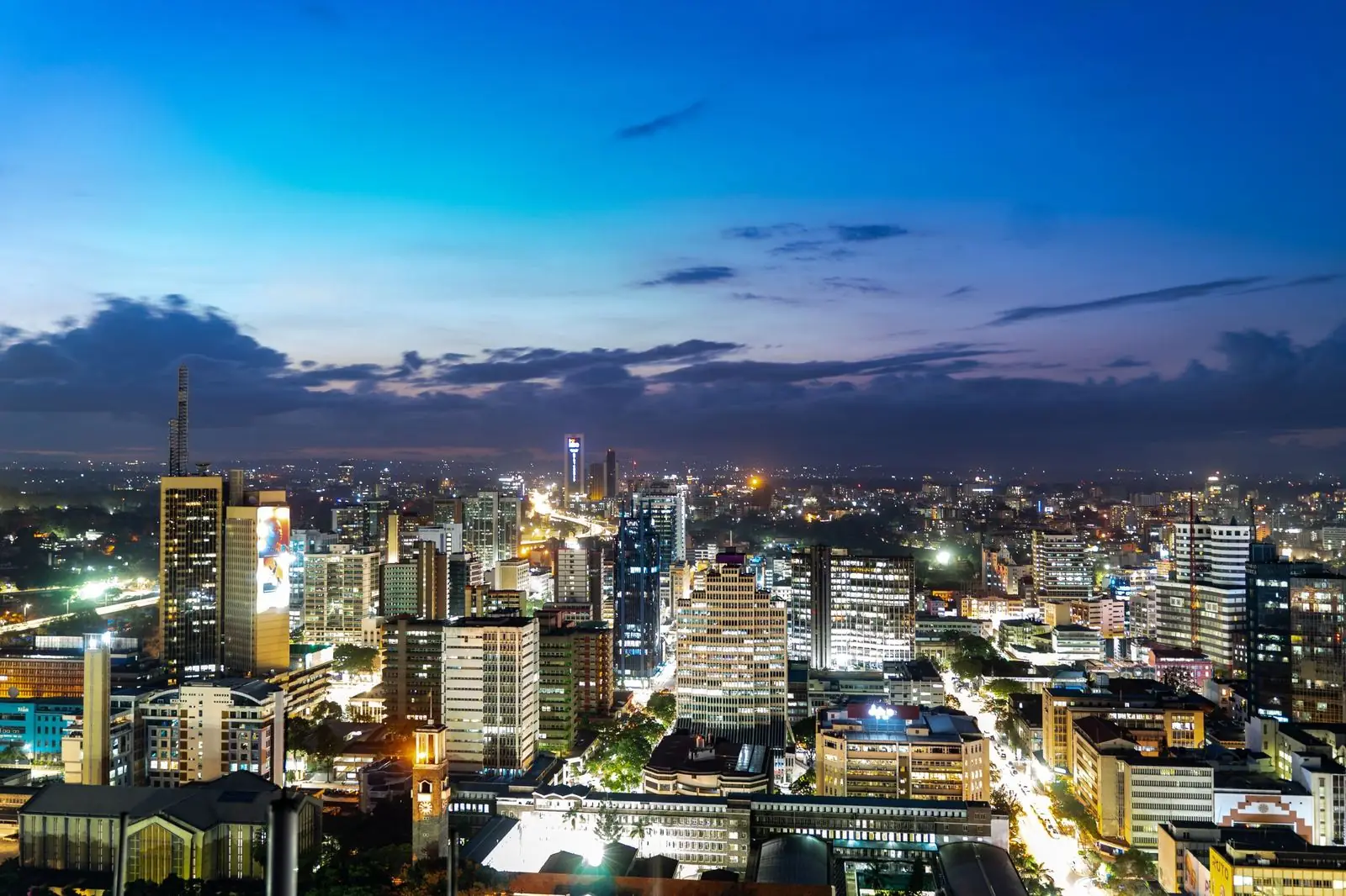 Nairobi city centre at dusk seen from above, office towers and lit streets under a deep blue sky