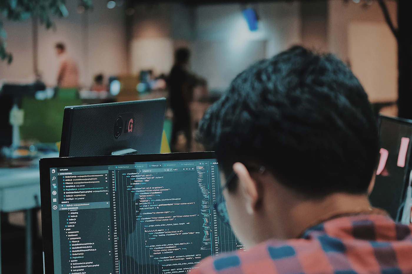 A technician at a monitor showing code and system windows in an open-plan office, representing managed IT support