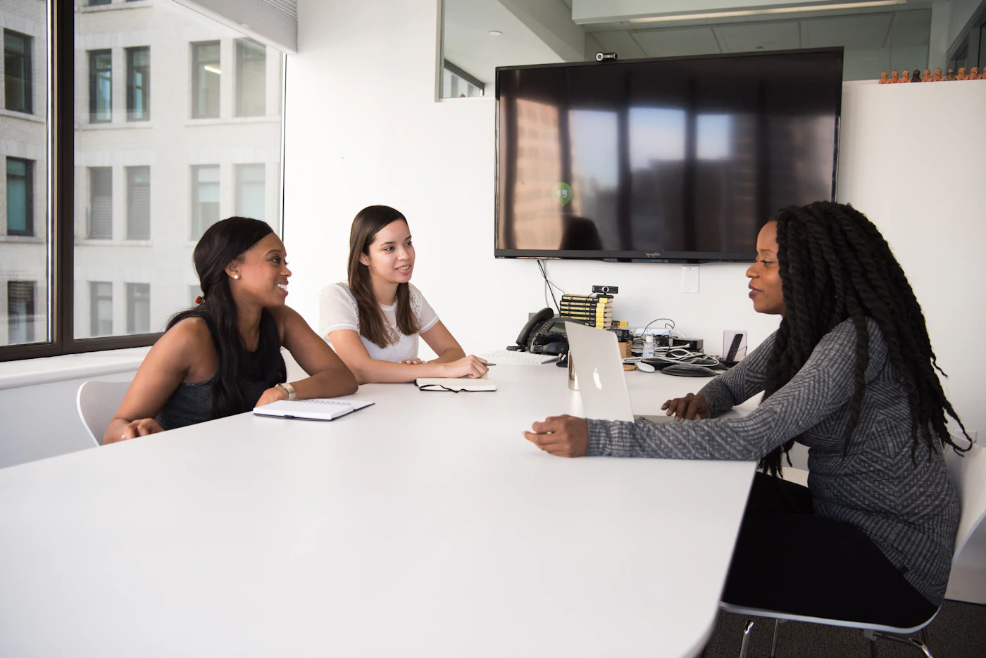 Three young professional women talking together around a table in a bright meeting room