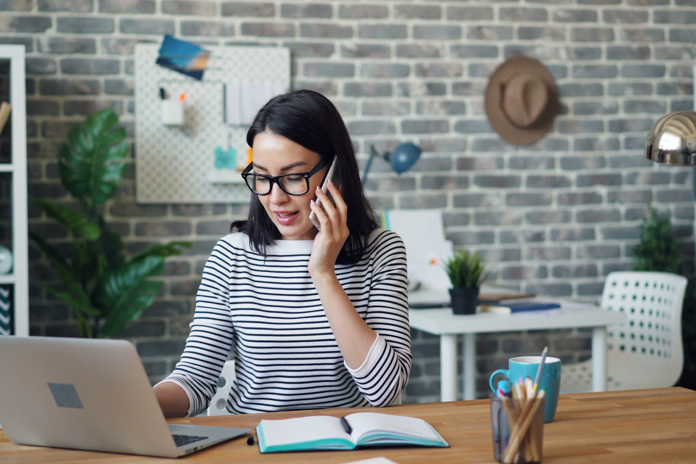 A woman on a phone call while working at a laptop in a plant-filled workspace, handling customer conversations across channels