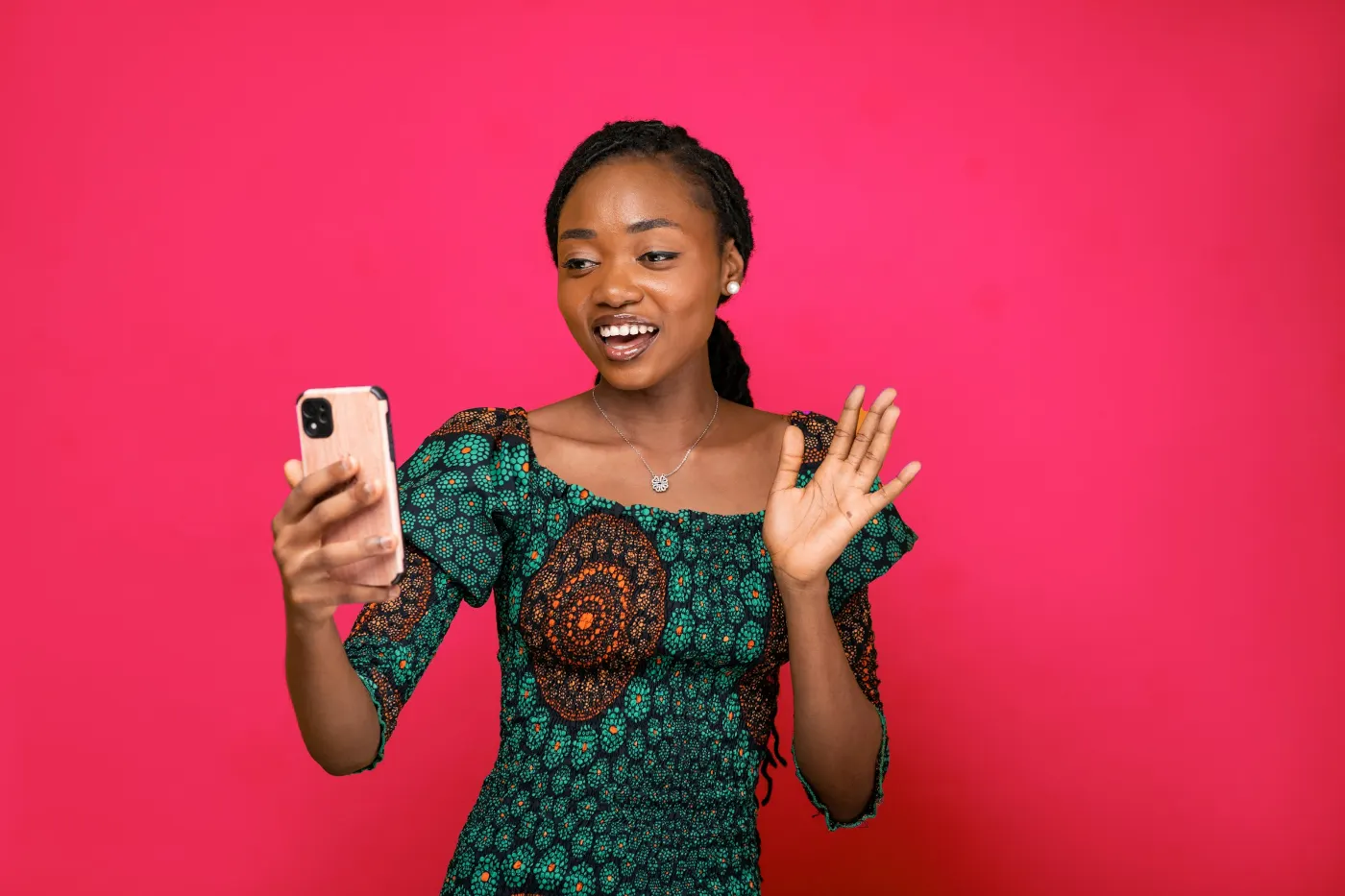 A woman recording social media content on her phone against a bright pink wall