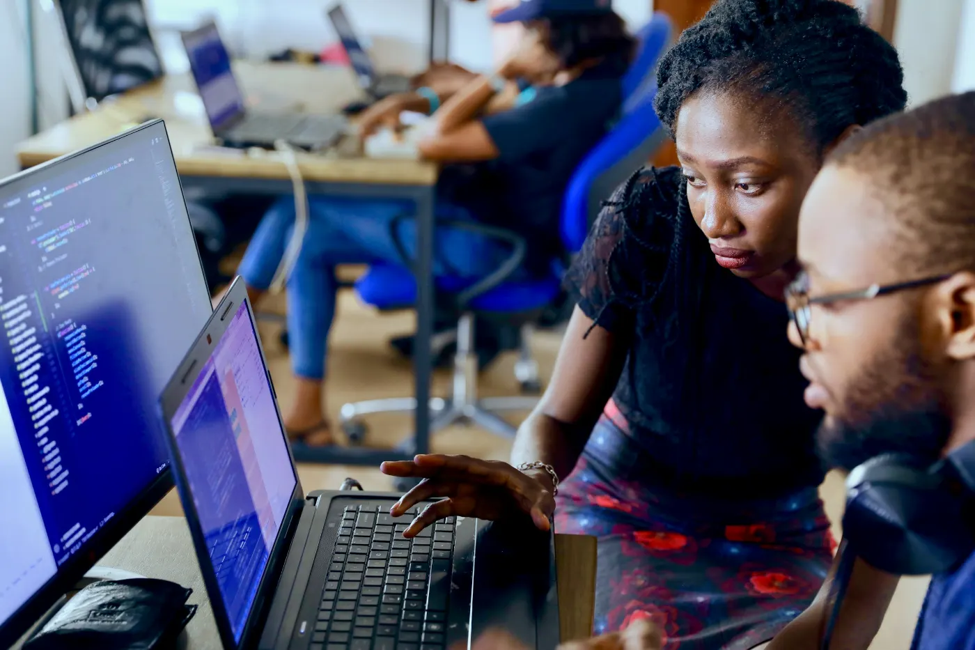 Young professionals working together at computers with data and code on their screens